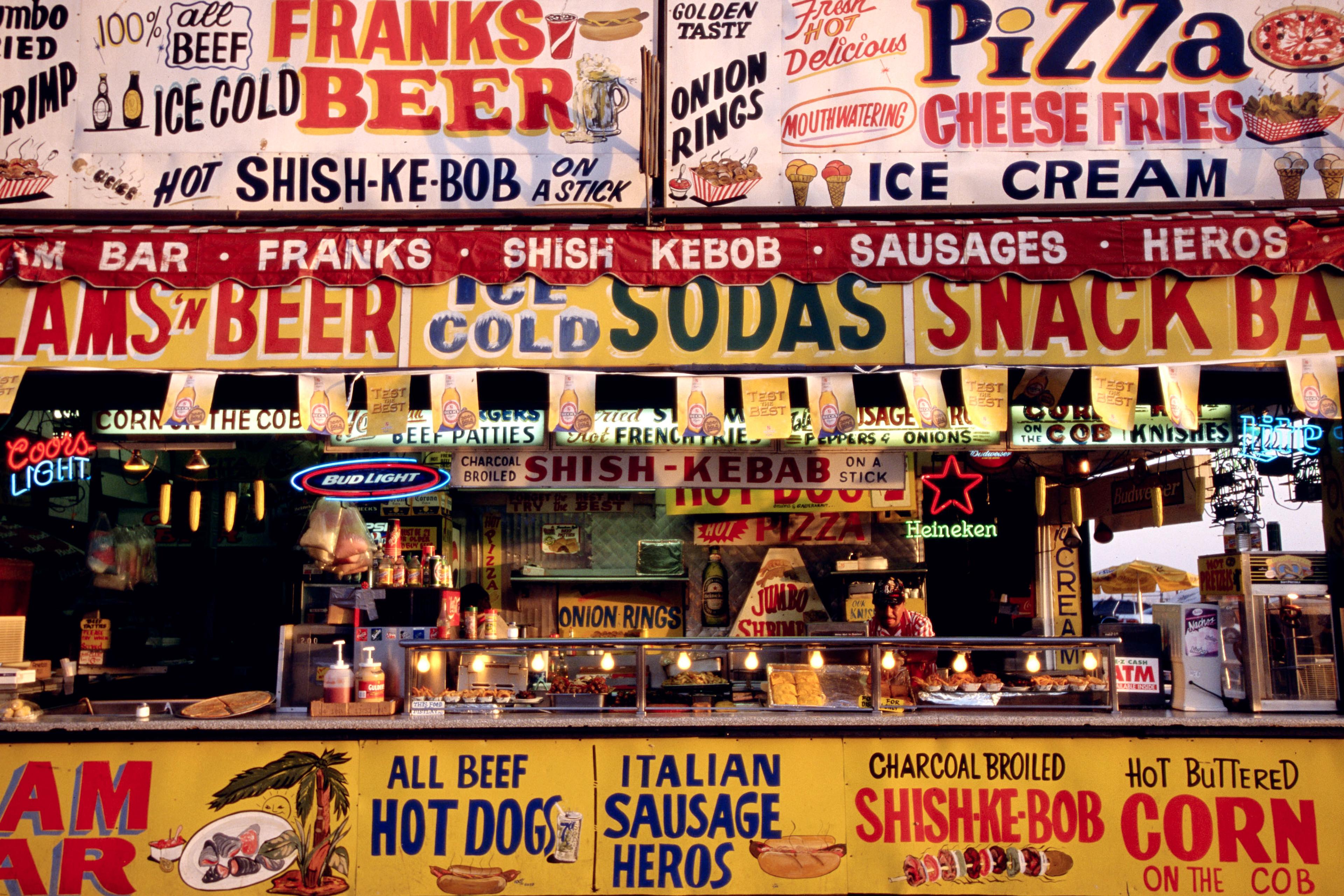 Photo of a vibrant snack bar with colourful signs advertising beer, pizza, sausages and ice cream.