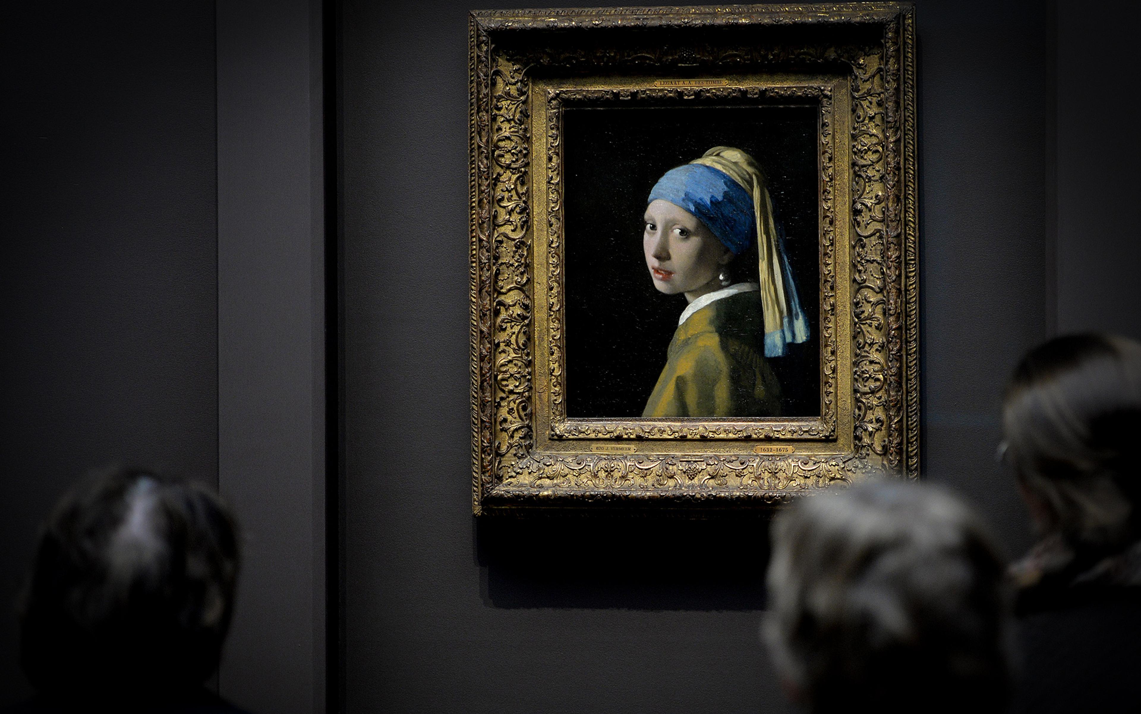 Painting of a girl with a pearl earring in an ornate frame, viewed by three people in a gallery setting.