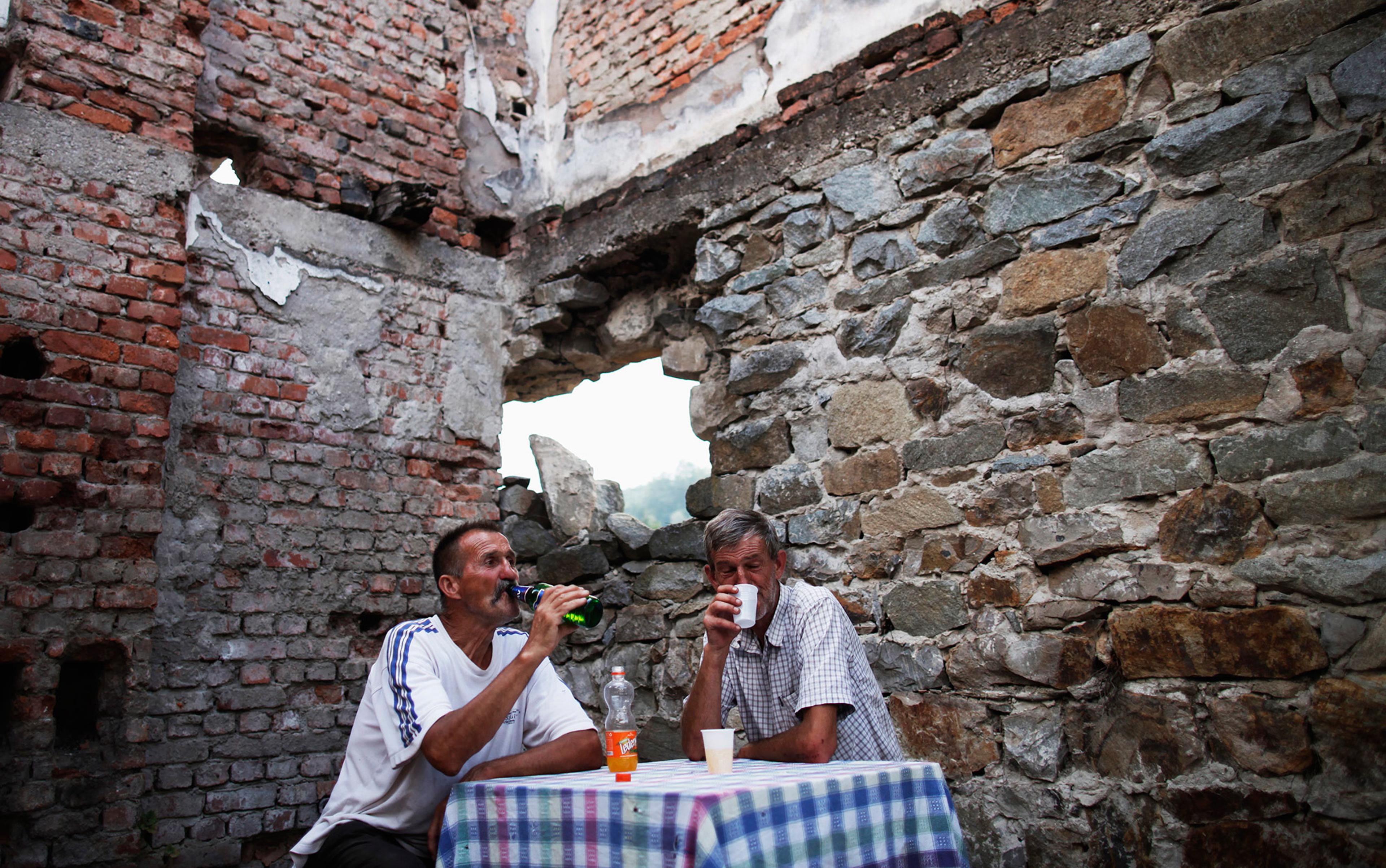 Two men sitting at a table with drinks in a rustic setting, surrounded by exposed brick and stone walls.