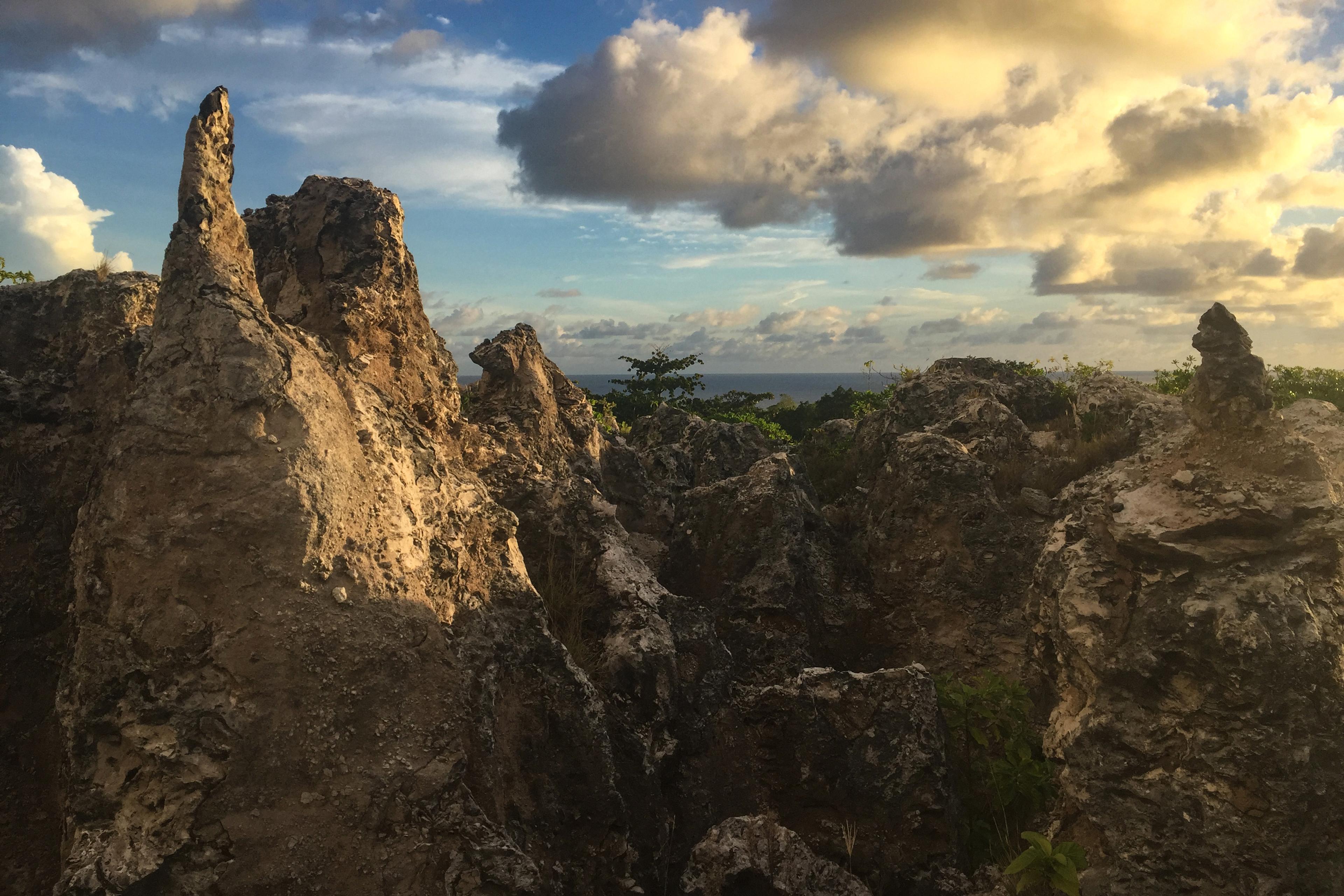 Photo of rugged limestone formations at sunset with a partly cloudy sky and sea visible in the background.