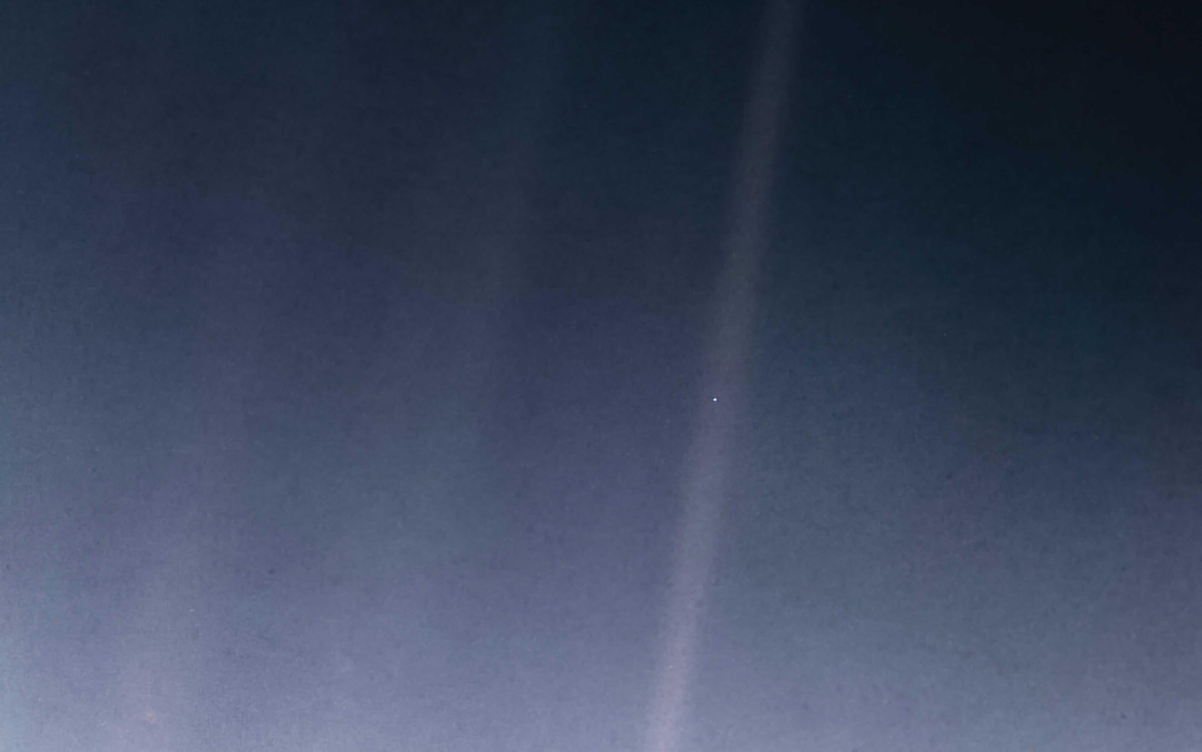 Photo of deep space with a pale blue dot in the distance against a dark background, featuring faint light streaks.