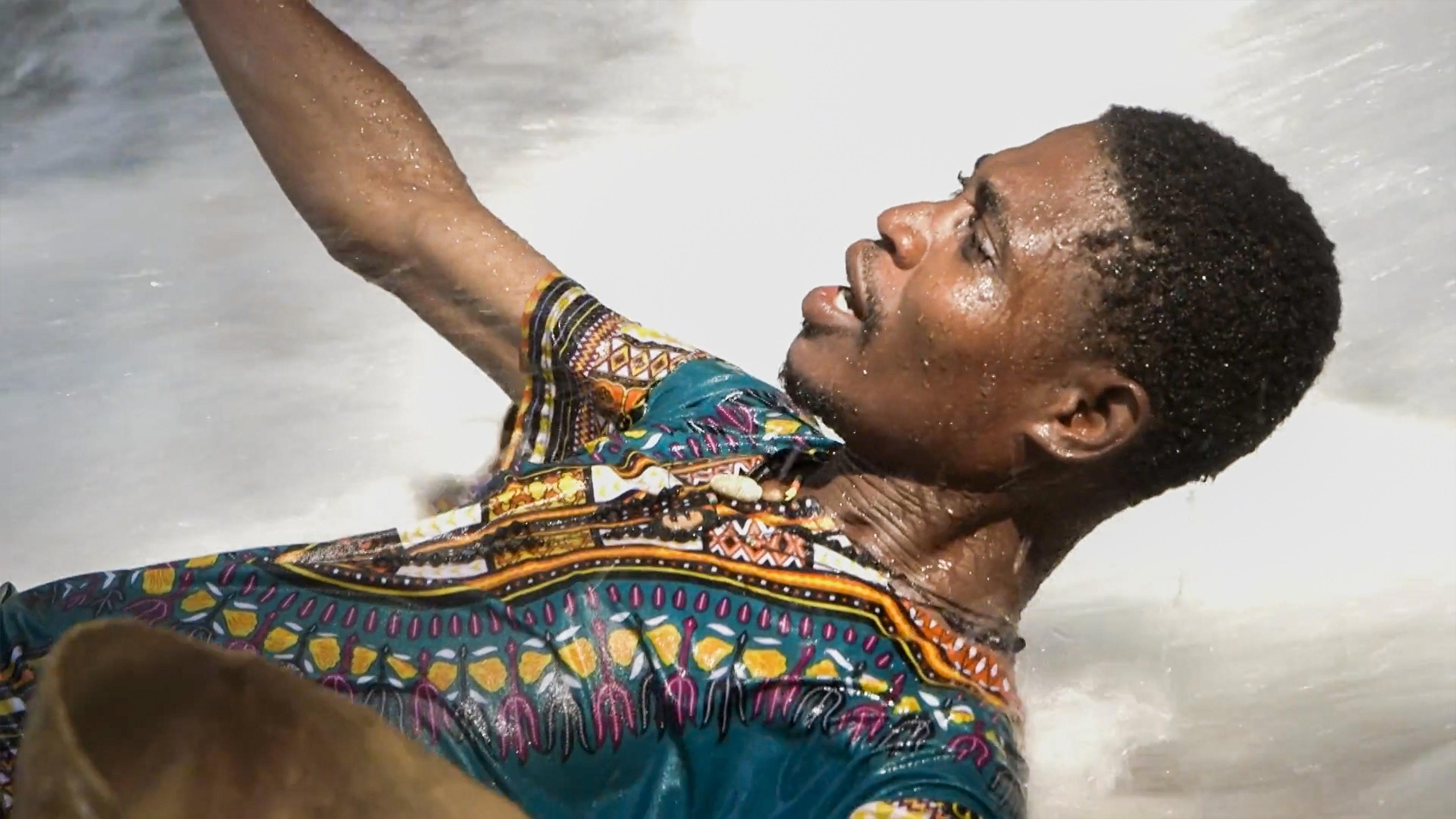Photo of a man in a colourful patterned shirt lying in water looking upwards with a focused expression.