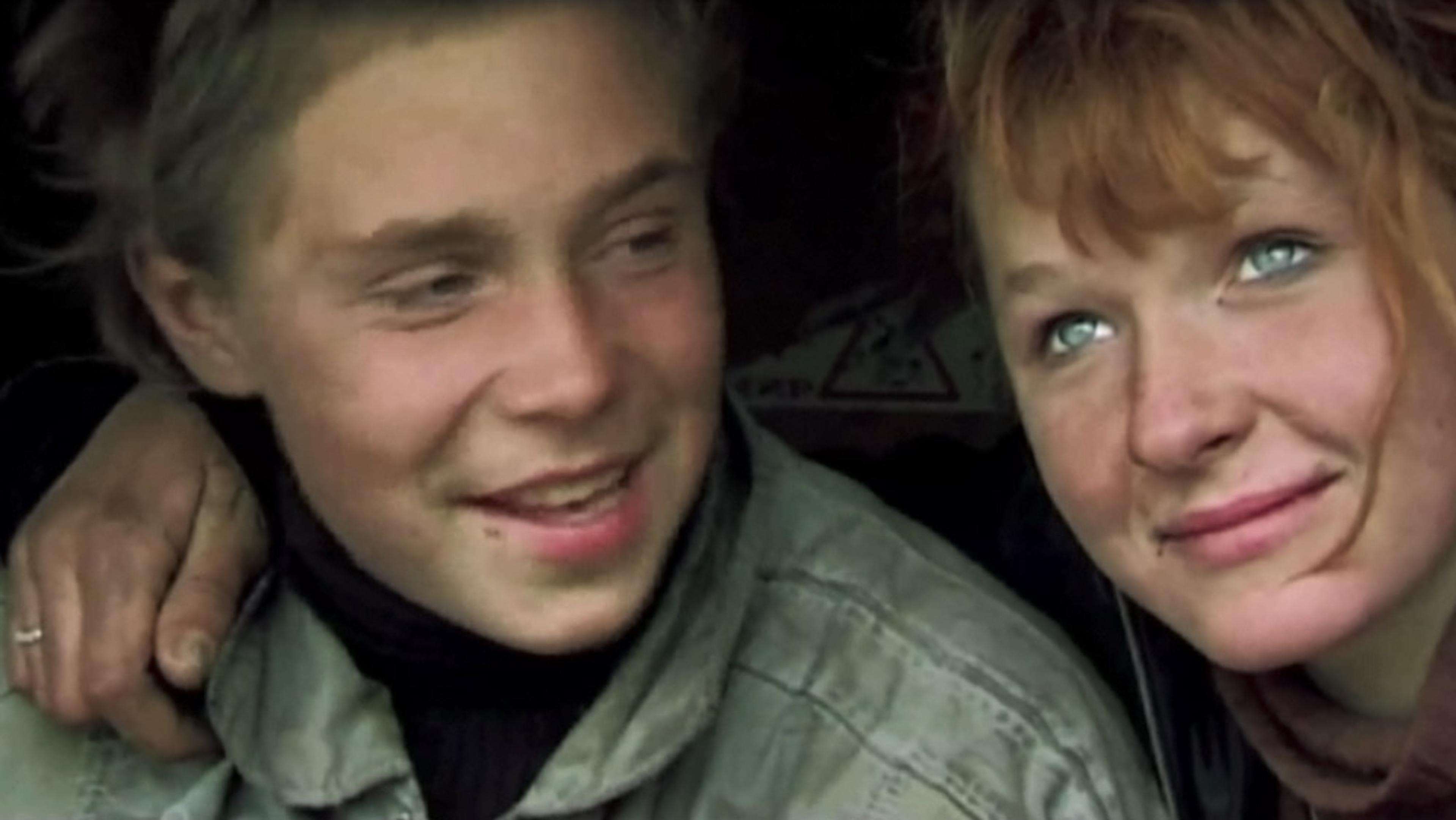 A young boy and girl smiling, with the girl’s arm around the boy’s shoulder, both looking content and relaxed.