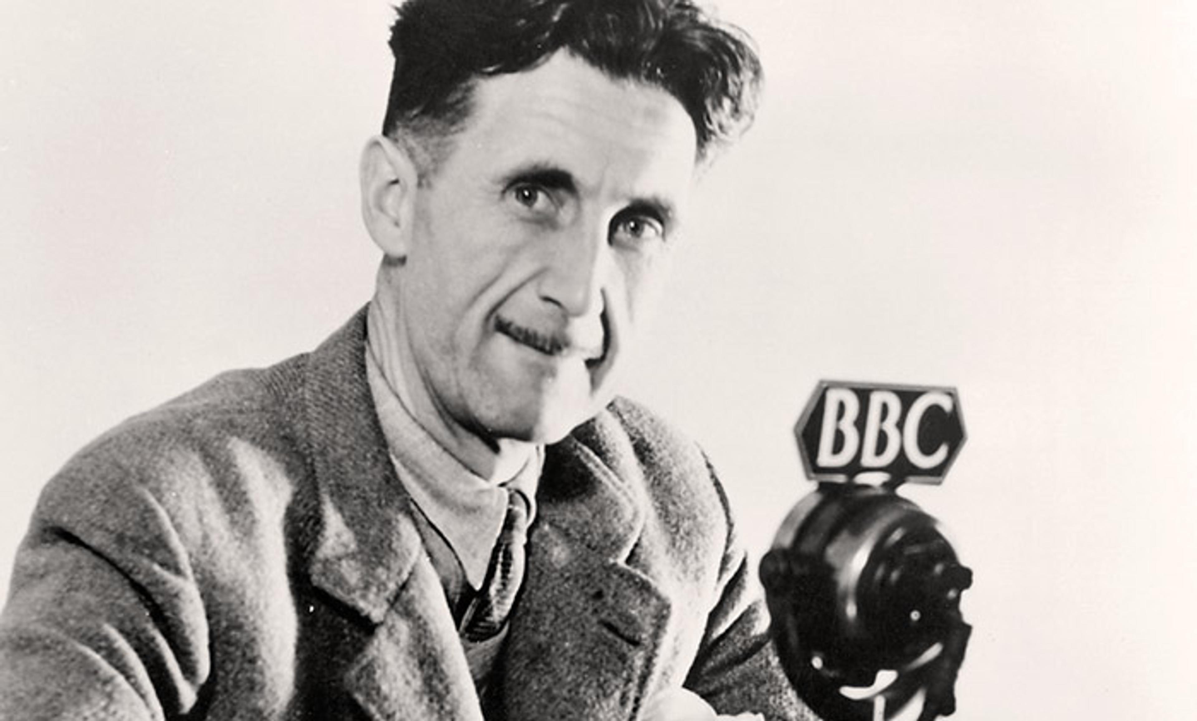 Black-and-white photo of George Orwell with a moustache and suit jacket speaking into a BBC microphone, appearing thoughtful and smiling.