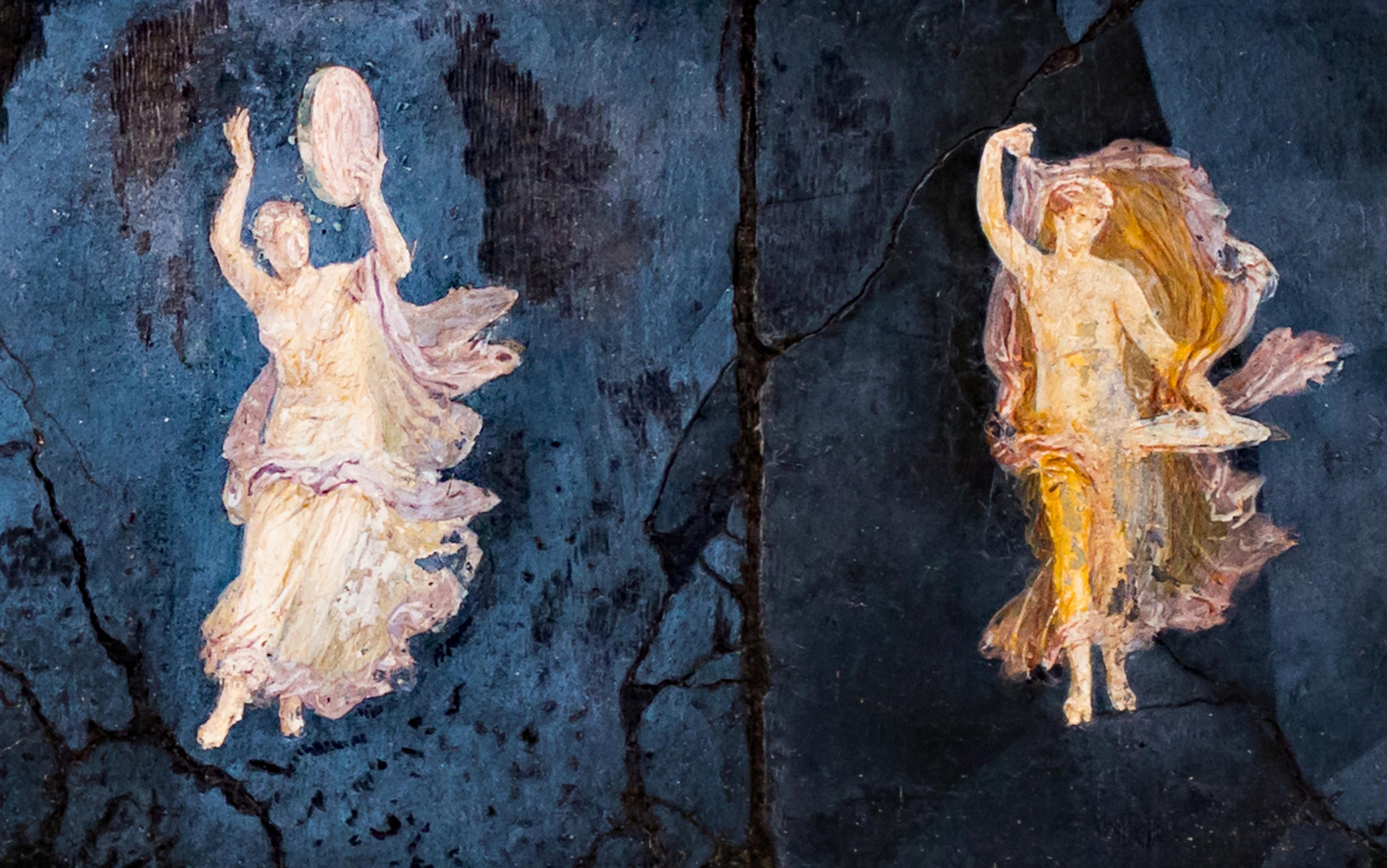Ancient fresco showing two figures in flowing robes dancing against a dark blue background, one holding a tambourine.