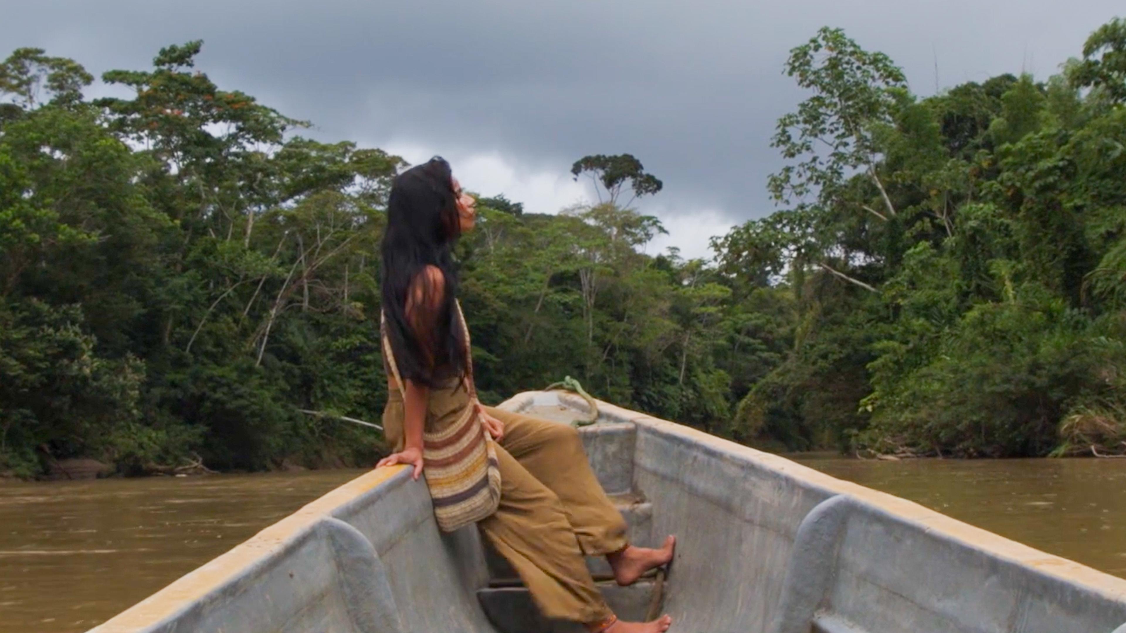Photo of a person sitting in a boat on a river surrounded by lush green jungle under a cloudy sky.